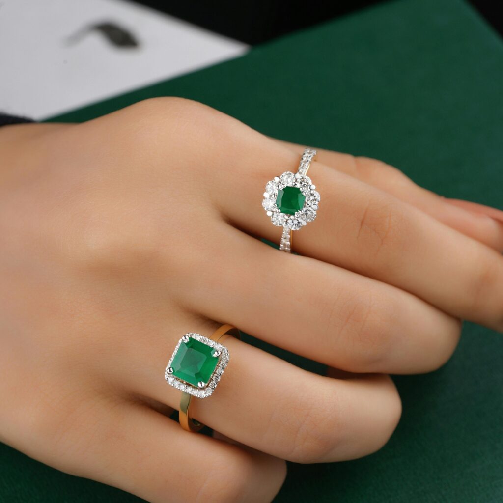 Close-up of elegant emerald and diamond rings worn on a hand, showcasing luxury jewelry.